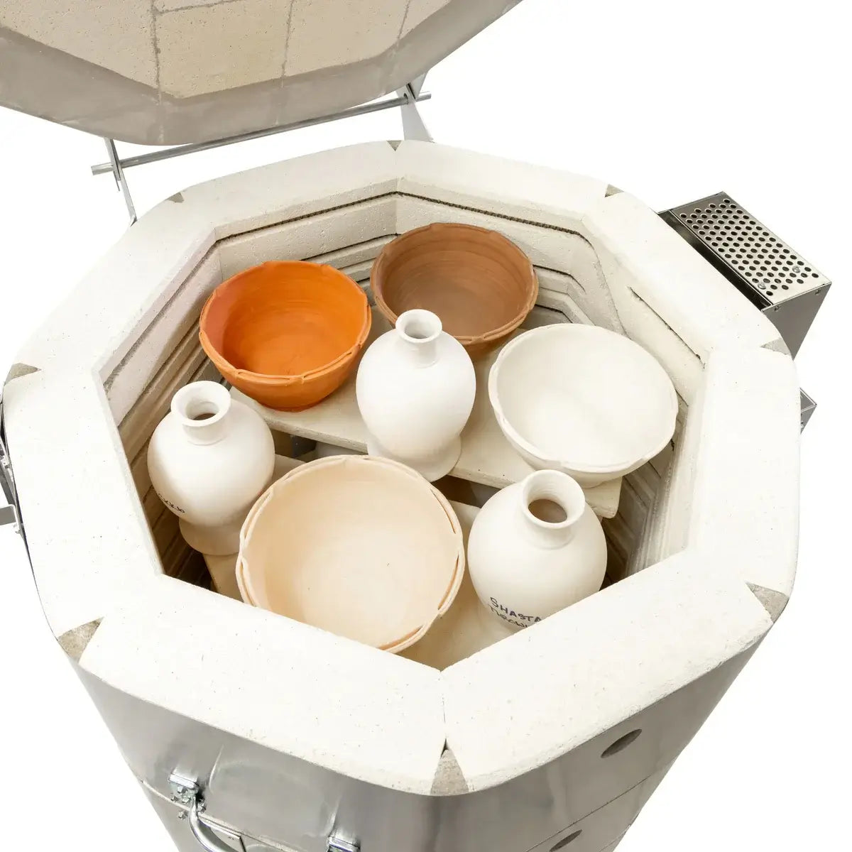 Vue du four à céramique ouvert avec des pots en terre et des bols en argile prêts pour la cuisson.